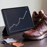 A digital tablet showing financial currency graphs next to a custom sneaker and leather swatches.